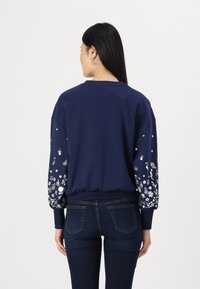 Marinblå sweatshirt med blommönsterbroderi på ärmarna, ribbad nederkant och manschetter, avslappnad passform, mjuk textur och rundad halsringning.