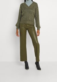 Maglione a collo a V in maglia testurizzata di colore verde oliva, abbinato a pantaloni a gamba larga in ecopelle lucida verde oliva e stivali alla caviglia neri con tacco.