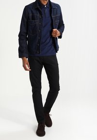 Takit denim tummansinisena, jossa on napitus edessä ja neljä taskua, käytetään laivaston sinisen polo-paidan päällä, yhdistettynä mustiin slim-fit-housuihin ja ruskeisiin kenkiin.