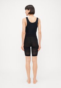 Top sem mangas preto e calções de ciclismo de cintura alta a condizer com um design texturizado e transparente nos calções. Material liso e elástico.