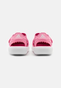 Un par de sandalias Adidas rosas con suelas blancas vistas desde la parte trasera sobre un fondo blanco.