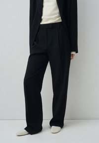 Pantalons navy à rayures fines, confectionnés dans un tissu lisse, avec une coupe largement évasée et des poches latérales, associés à un haut beige et des chaussures claires.