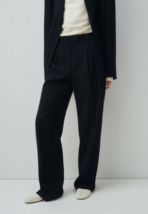Tailored navy pinstriped trousers made from a smooth fabric, featuring a wide leg design and side pockets, paired with a beige top and light shoes.