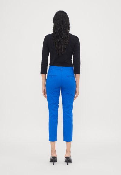 Pantalons blue cropped avec une texture lisse, présentant deux poches arrière et un style ajusté, assortis à un haut noir à manches longues.