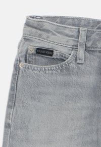 Ljusgrå denimjeans med en framficka och en svart Calvin Klein-etikett. Har silverfärgade detaljer och en klassisk femficksdesign.