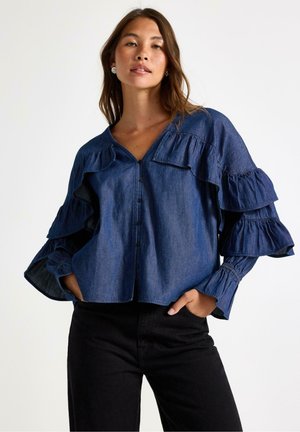 Denim-pusero, jossa on röyhelöhihoja, syvä V-pääntie ja etupainikkeet. Tumma sininen väri, jossa on sileä tekstuuri ja ker gathered cuffs.