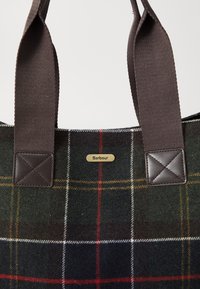 Geantă din țesătură carourile, cu mânere robuste de culoare brun închis și un mic tag metalic aurie cu logo-ul Barbour, amplasat centrul între mânere.