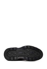 Semelle de sneaker noire avec caoutchouc texturé, présentant des motifs de traction distincts et des détails de logo circulaire proéminents. Design plat et robuste.