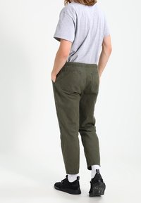 Pantalones de algodón verdes con un corte relajado, bolsillos traseros visibles, combinados con una camiseta gris y zapatillas negras. Modelo de espaldas, mostrando el diseño.