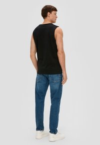 Zwarte mouwloze top gecombineerd met blauwe jeans, wat een ontspannen pasvorm benadrukt. Witte sneakers maken de outfit af. Textuur en stiksels zijn zichtbaar.