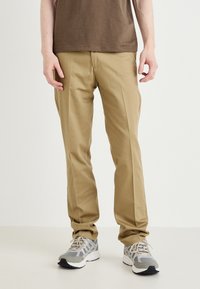 Beige chinos with a tailored fit, featuring a flat front and side pockets, paired with gray and white athletic shoes.