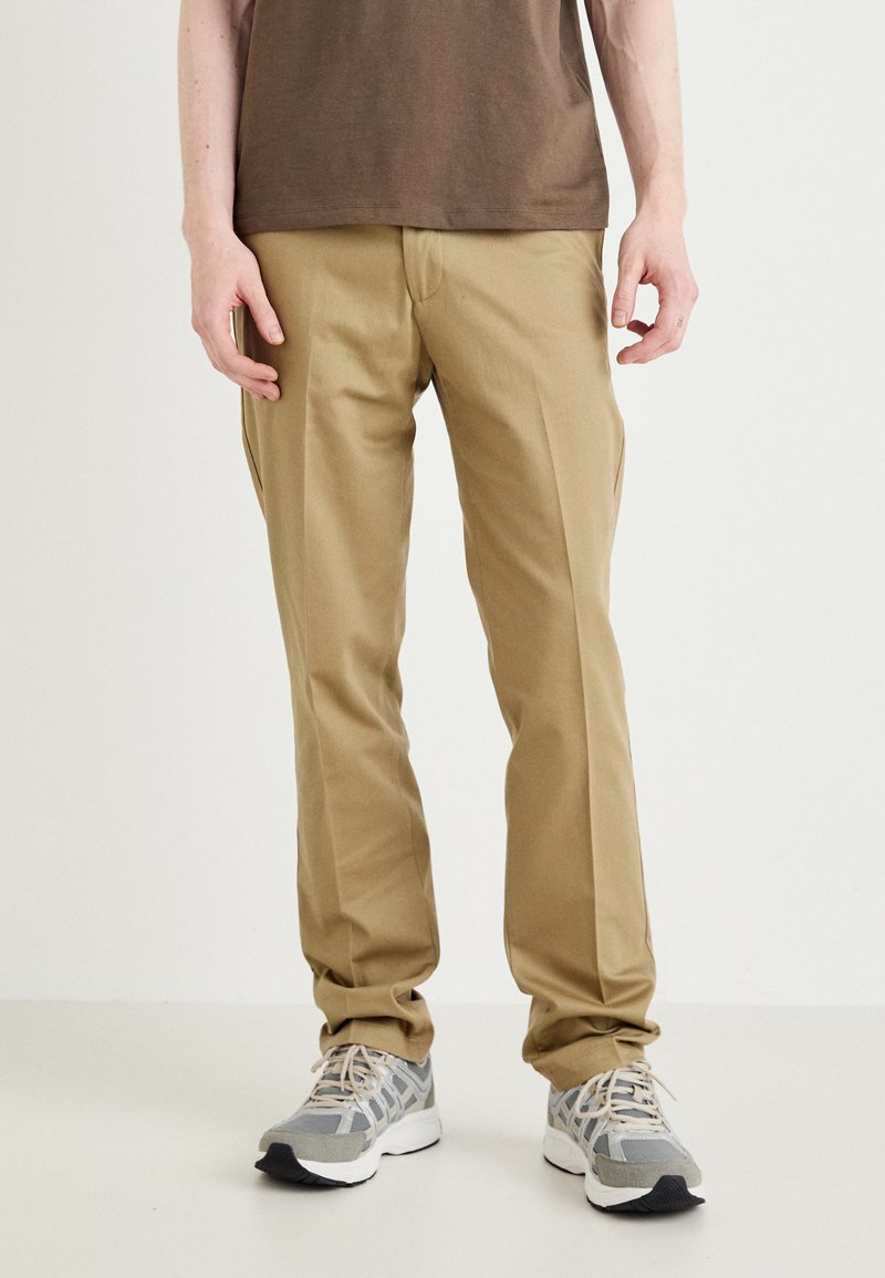 Beige chinos with a tailored fit, featuring a flat front and side pockets, paired with gray and white athletic shoes.