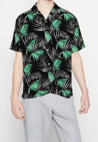 Kortärmad skjorta med svart bakgrund, med ett mönster av gröna och vita palmblad. Knappar och en avslappnad passform.