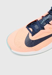 Šviesiai rožiniai sportiniai bateliai su kvėpuojančia tinklelio viršutine dalimi, tamsiai mėlynomis raišteliais ir tekstūriniu juodu Nike logotipu. Yra baltas vidurinio pado sluoksnis ir akvamarino spalvos padas.