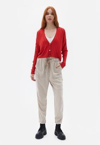 Rød ribbet cardigan med v-hals og knaplukning, parret med beige løstsiddende bukser med to forlommer, komplementeret af sorte støvler.