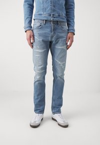 Ljust blå ripped jeans med rak passform, slitna detaljer och en klassisk femfickdesign, parat med vita sneakers.