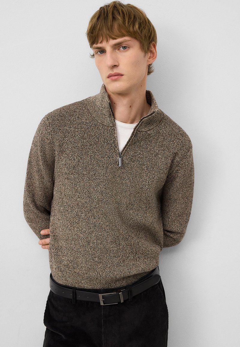 Bruine gebreide pullover met ritskraag, voorzien van een textuurpatroon. Gecombineerd met zwarte corduroy broek en een zwarte riem.