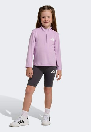 Lilla langærmet pullover med halvdelt lynlås, parret med grå cykelshorts. Begge har Adidas-logo på. Hvide sportsko fuldender looket.