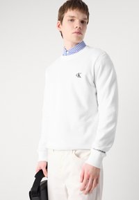 Sudadera blanca de cuello redondo hecha de algodón, con un logotipo bordado en negro "CK" en el pecho y "Calvin Klein Jeans" impreso en el puño.