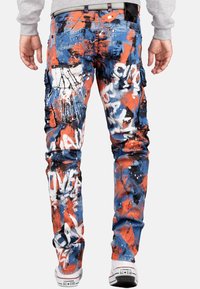 Pantalons cargo camouflés avec un design éclaboussures de peinture bleue, orange et blanche. Présente plusieurs poches et une silhouette de jambe ajustée.