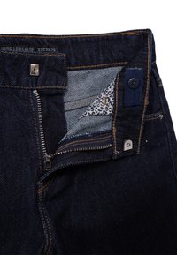 Vaqueros de mezclilla oscuros de pierna ancha con cremallera plateada, cierre de botón y forro de bolsillo de estampado de leopardo en contraste. Detalles de costura a lo largo de los bordes.