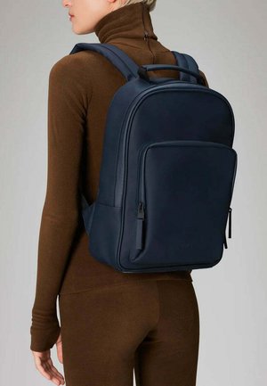 Zaino in pelle blu navy con design strutturato, tasca frontale con zip e spallacci imbottiti. Estetica elegante e minimalista.
