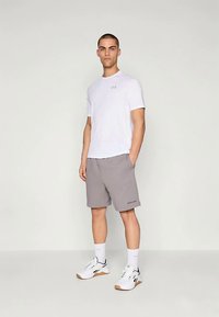 Valge sportlik t-särk halli logoga, koos hallide lühikeste pükstega, millel on küljetaskud, ja valged spordijalatsid mustade detailidega.