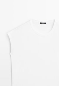 Sleeveless white crew neck shirt with a black brand label sewn inside the collar.