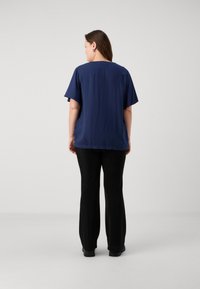 Blouse bleu marine à manches courtes, ample, en tissu lisse, associée à un pantalon large noir avec une légère brillance.