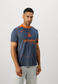 Maillot de football bleu foncé avec des accents orange. Il présente un design à col en V, un logo Nike, un branding Betsson et des manches courtes en tissu respirant.