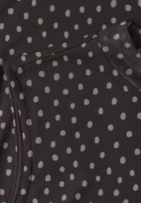 Tissu noir à petits pois blancs, montrant une couture détaillée et un bord froncé sur un matériau texturé.