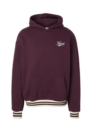 Tumepunane kapuutsiga pusajakk esitasku ja valge "Kani" logoga rinnal, valgete triipudega varrukate otstes ja ääres.