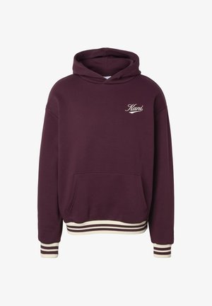 Tumepunane kapuutsiga pusajakk esitasku ja valge "Kani" logoga rinnal, valgete triipudega varrukate otstes ja ääres.