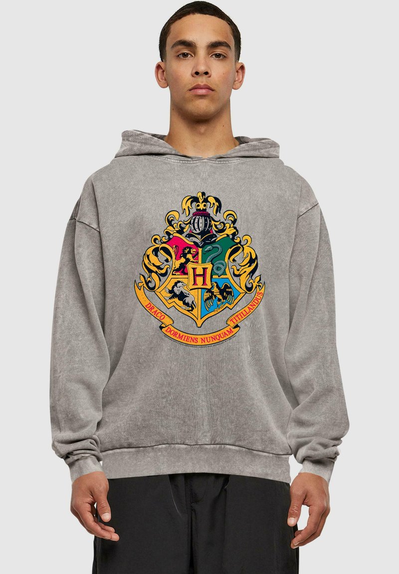Sudadera con capucha gris que presenta un colorido escudo bordado de Hogwarts con varios símbolos, contorneado en amarillo y con una banda debajo.