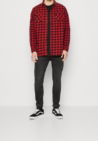 Rutig flanellskjorta i röd och svart med två bröstfickor, tillsammans med svarta jeans och svarta sneakers med vita sulor.