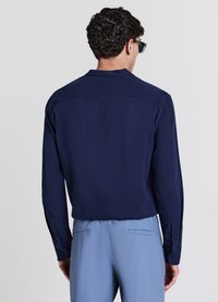 Chemise bleu marine à manches longues avec un tissu texturé et un col rond, associée à un pantalon bleu clair avec des poches arrière.
