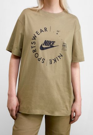 Olivengrøn bomuld t-shirt med korte ærmer, der har et sort Nike-logo, cirkulær tekst og grafiske elementer. Enkel, afslappet pasform.