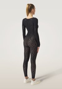 Body en dentelle noire avec manches longues, coupe ajustée et motif texturé. Associé à des baskets blanches, vue de dos.