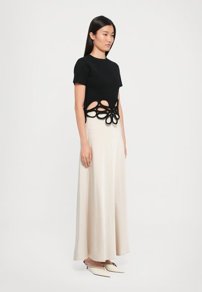 Black short-sleeve top with a cut-out floral design at the waist paired with a flowing cream skirt and pointed white shoes. Smooth textures.