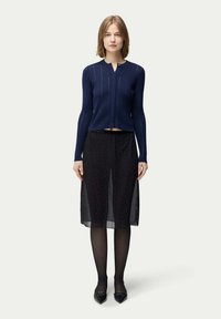 Marinblå ribbad stickad cardigan med rund hals och framknäppning, parat med en svart genomskinlig kjol med små, spridda rhinstenar.