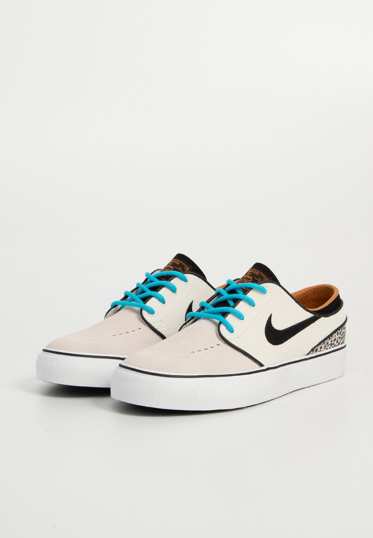 Zapatillas de skate blancas y beige con acentos negros, cordones turquesa y un patrón texturizado en el talón. Suave ante y suela de goma.