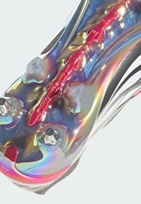 Bota de fútbol con un upper brillante e iridiscente, que presenta un acento rojo "Powerframe" y tacos plateados sobre una suela gris.