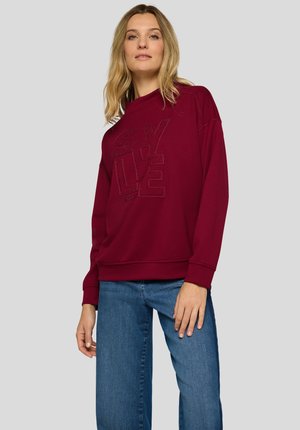 Weinroter Pullover mit gerippten Bündchen und Saum, mit einem strukturierten "STYLE"-Aufdruck. Kombiniert mit hellblauen, gerade geschnittenen Jeans.