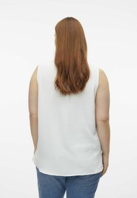 Haut sans manches blanc avec un tissu texturé, présentant un ourlet arrondi. Le dos montre des lignes fluides et une coupe décontractée, associé à un jean bleu.