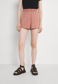 Světlé růžové šortky s elastickým pasem a volným střihem, spárované s černými sandals s pásky, které mají hroty a spony.