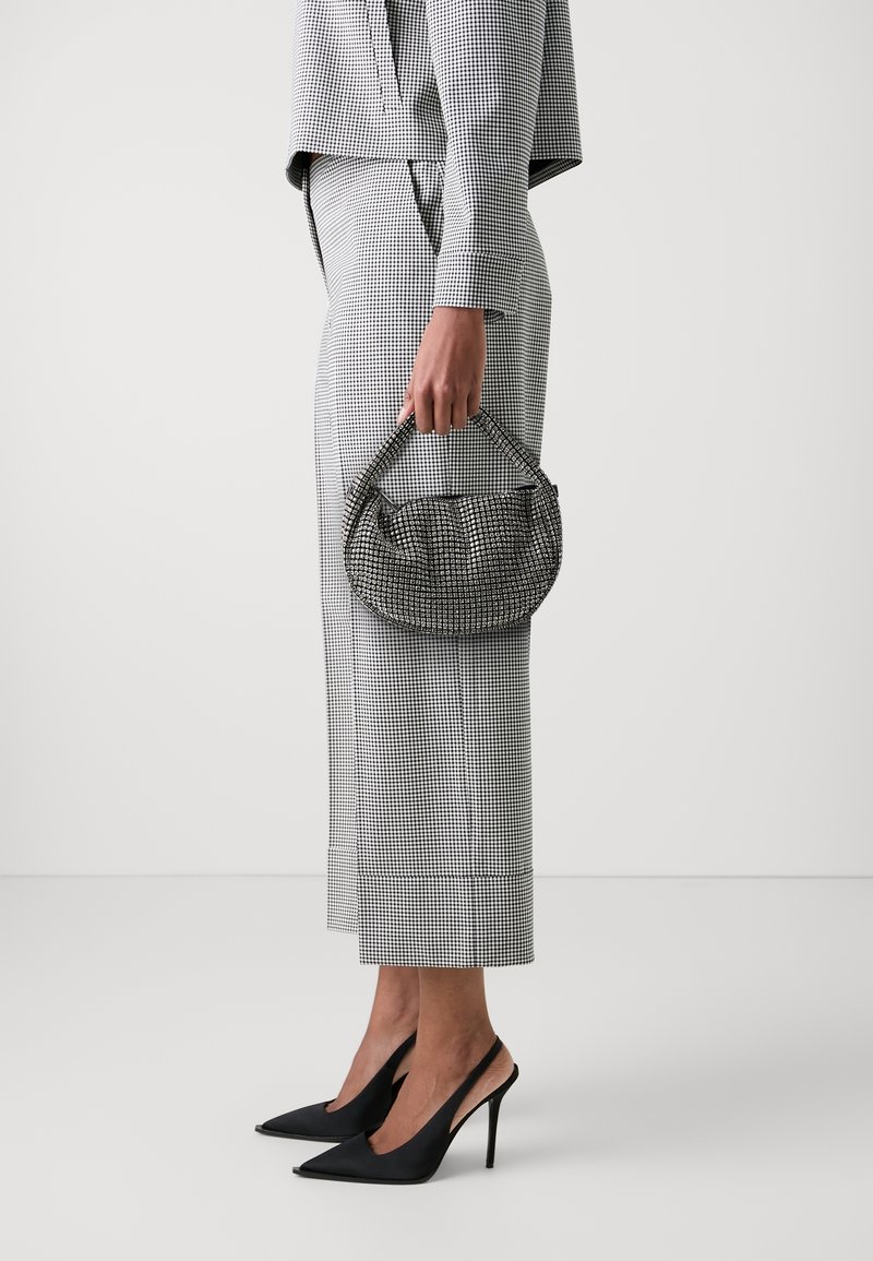 Personne tenant un petit sac à main noir et blanc à carreaux, portant un tailleur-pantalon à carreaux assorti et des chaussures slingback noires à talons hauts.