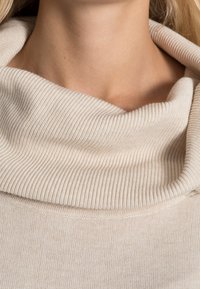 Beige Rollkragenpullover mit gerippter Struktur und glatter Oberfläche. Weicher Stoff mit einem lockeren Sitz am Ausschnitt und den Schultern.