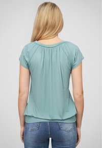 Lichtblauwe top met korte mouwen en een geplooid detail aan de achterkant, gemaakt van zachte stof. Gedragen met strakke blauwe jeans.