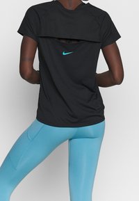 Svart atletisk t-shirt med blå Nike-logotyp, har en lager-på-lager-design och en utskärning på ryggen. Kombineras med ljusblå leggings.