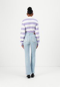 Osoba u ljubičastoj i bijeloj prugastoj majici dugih rukava s svijetloplavim visoko-strukiranim trapezicama i crnim cipelama s potpeticom, okrenuta prema van.